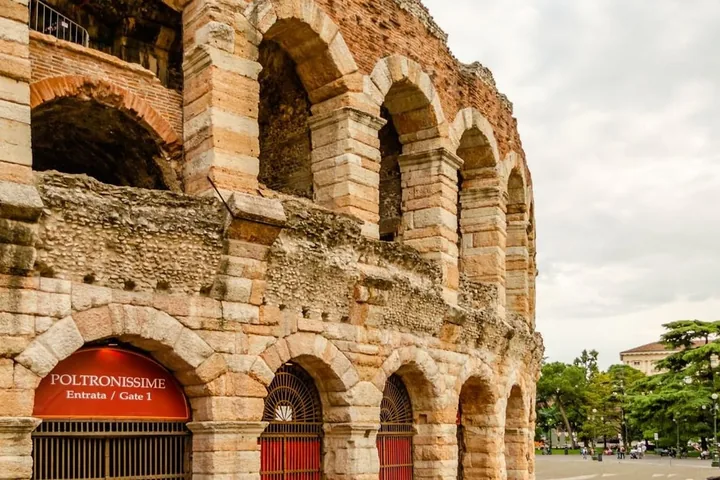 An arched entrance of the Arena di Verona with a red sign reading Poltronissime, Entrata Gate 1